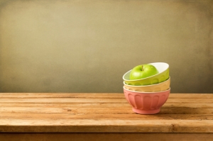 Colorful bowls with apple on wooden table